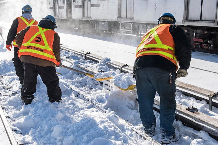 Construction workers clearing snow off of a railroad track.