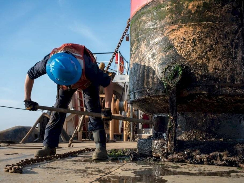 A construction worker turning the bottom of an barrel with a long handle.