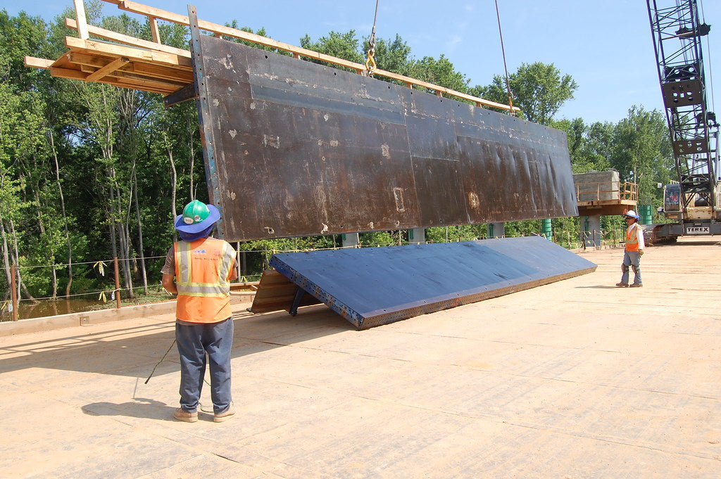 Two constructions workers guiding wood planks down from a crane attachment.