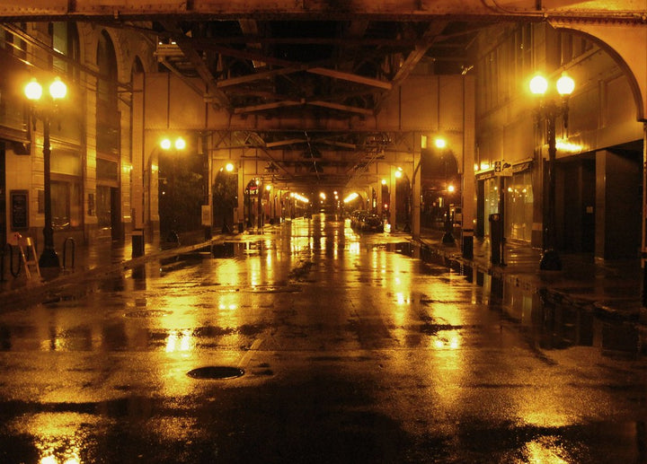 An empty, dark, city street filled with yellow street lights.