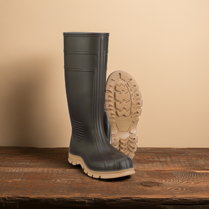 Green rubber boot with beige sole on a wooden surface and beige background