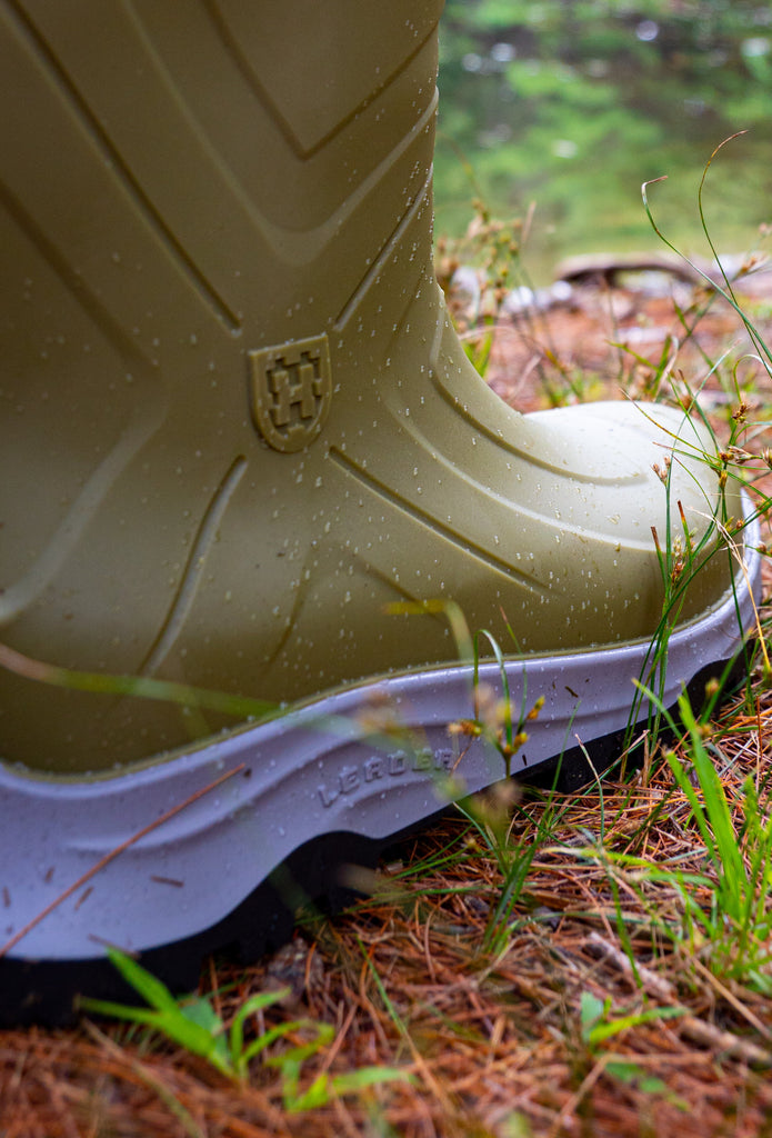 Green rubber boot on a natural background with water and greenery.