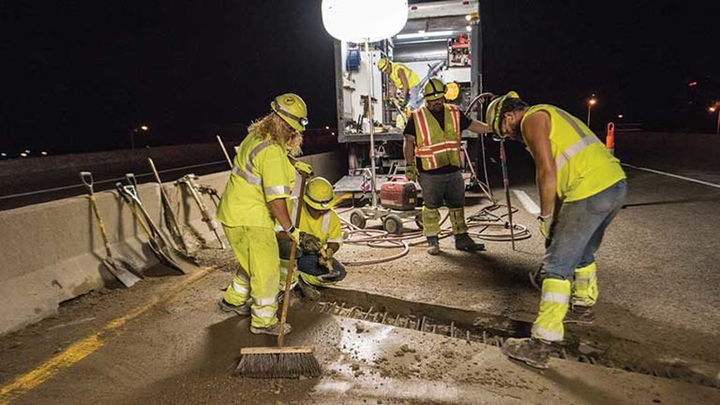 Construction workers sweeping debris off of a new road.