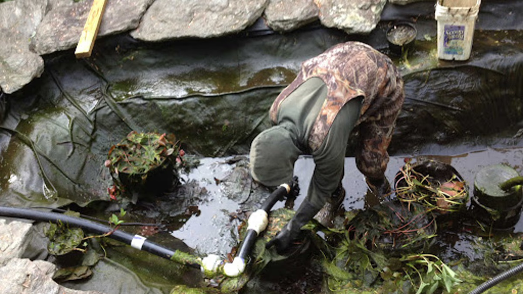 A man working on an empty pond's water pump/filter.