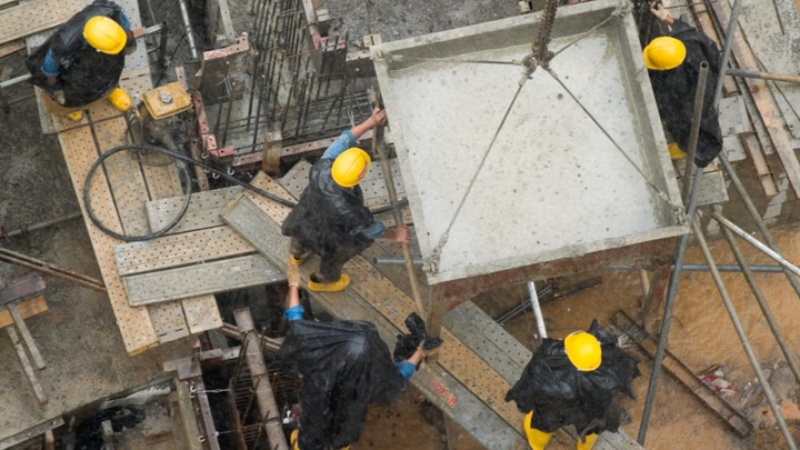 Construction workers guiding a crane that is holding a large piece of concrete.