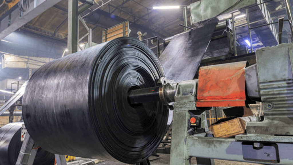 A wheel of rubber being rotated and layered onto by a machine in a factory.