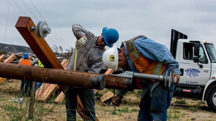 Two construction workers putting screws into a beam.