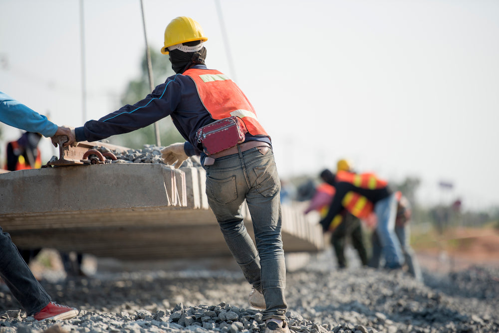 Construction workers guiding a large piece of a concrete controlled by a crane.